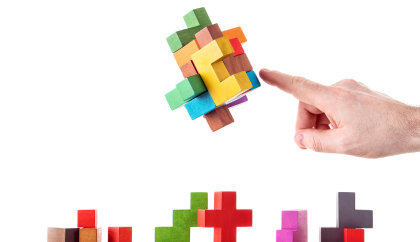 A hand pointing at a colorful wooden puzzle cube made up of smaller cubes of different colors